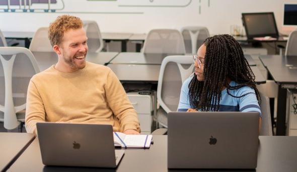一名女学生和一名男导师在办公室看着笔记本电脑时笑了起来.